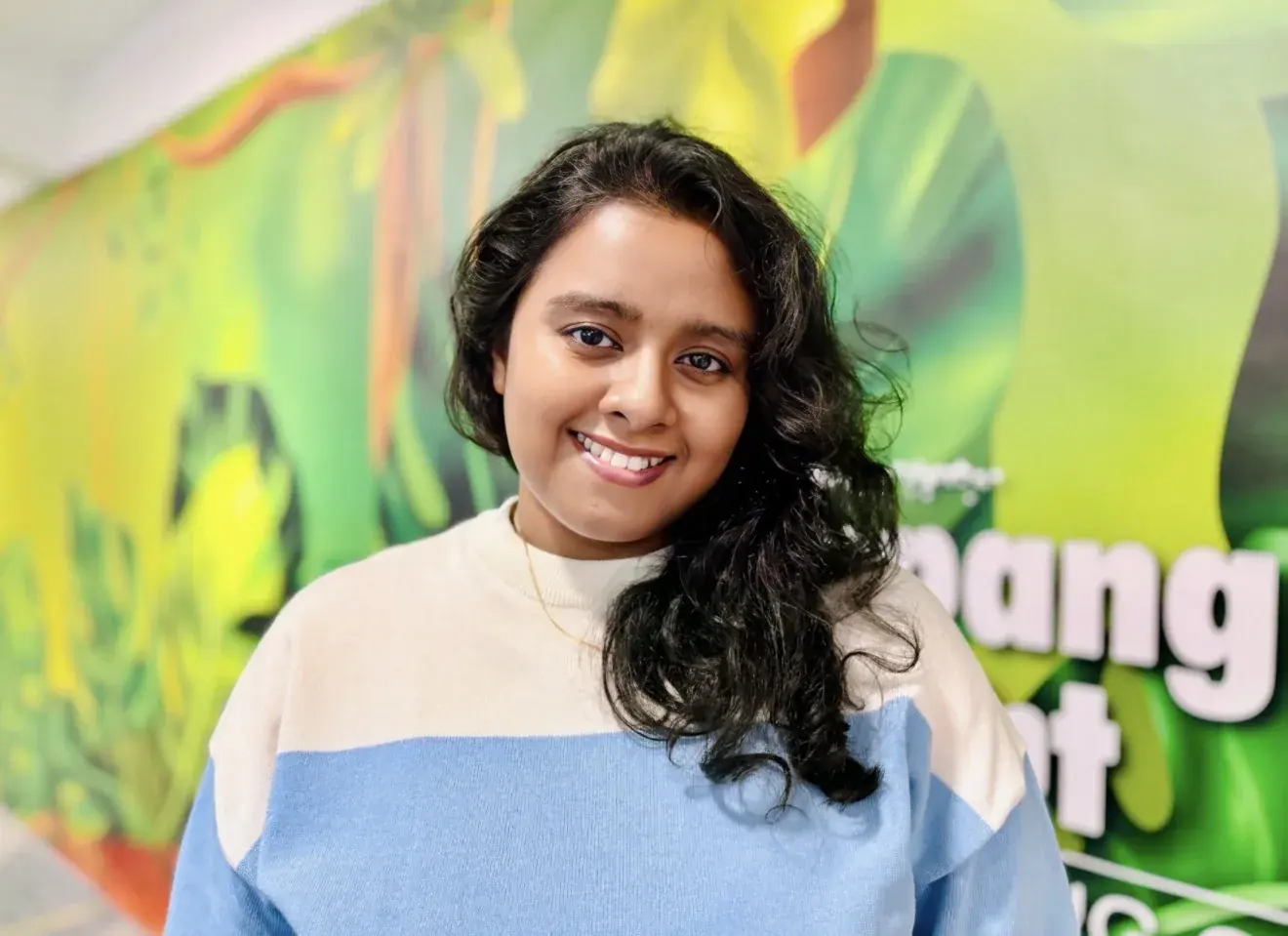 Adrita smiling in front of a bright green background